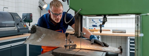 A tradesperson is cutting a metal sheet on a cutting machine in a workshop.