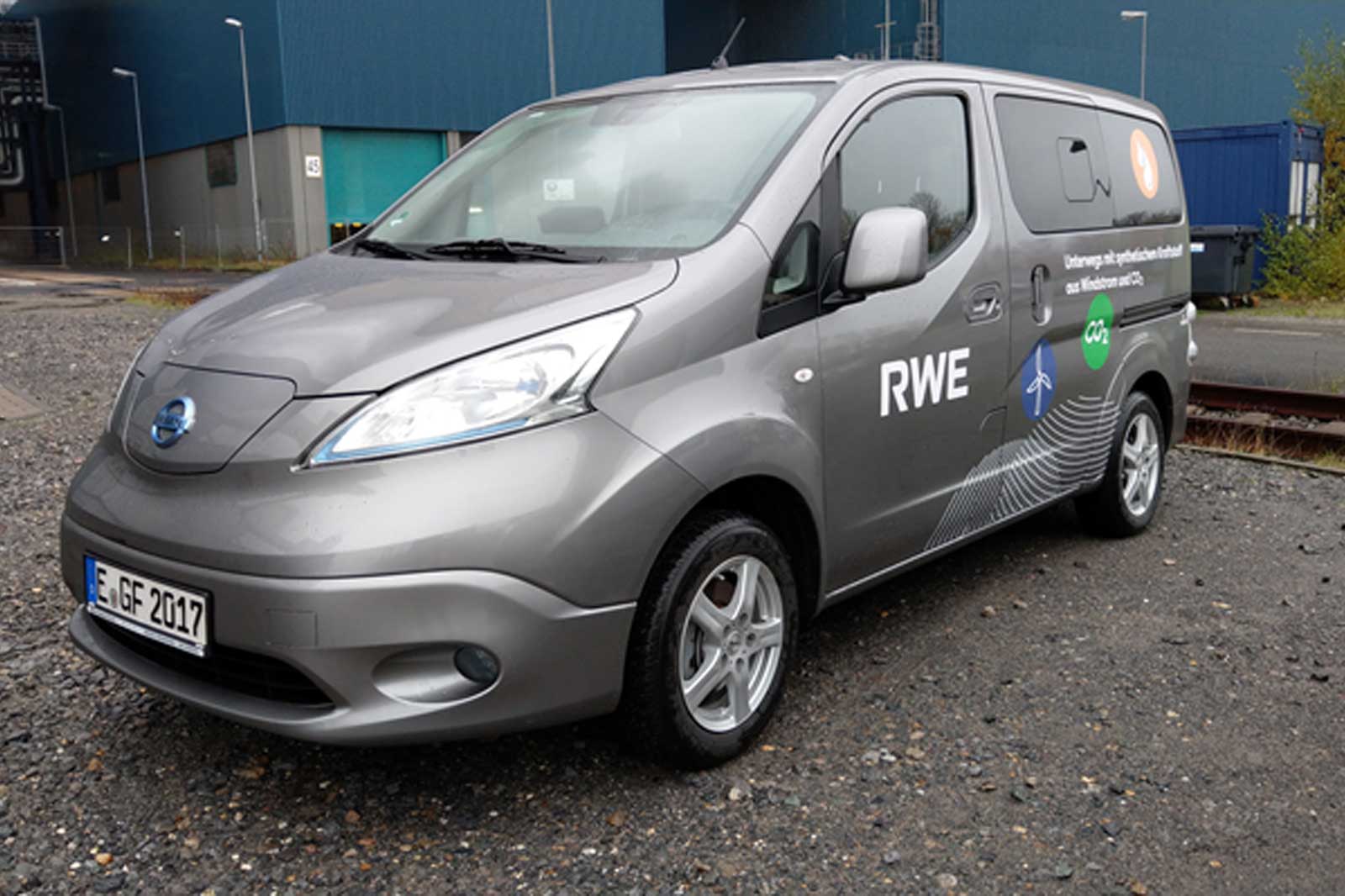 Ein grauer Lieferwagen von Nissan mit RWE-Logo steht auf einer Schotterfläche vor einem Industriegebäude.