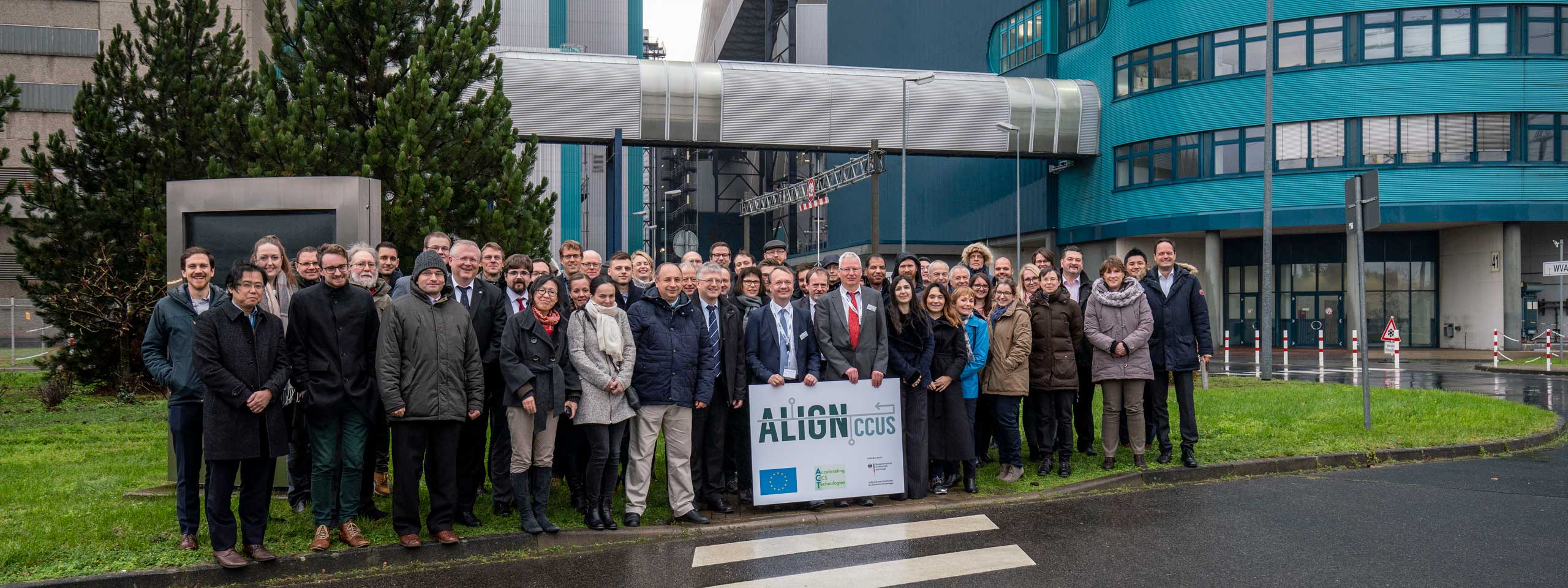 Eine Gruppe von Menschen posiert im Freien und hält ein Schild mit der Aufschrift ALIGN CCUS, mit einem modernen Gebäude im Hintergrund.