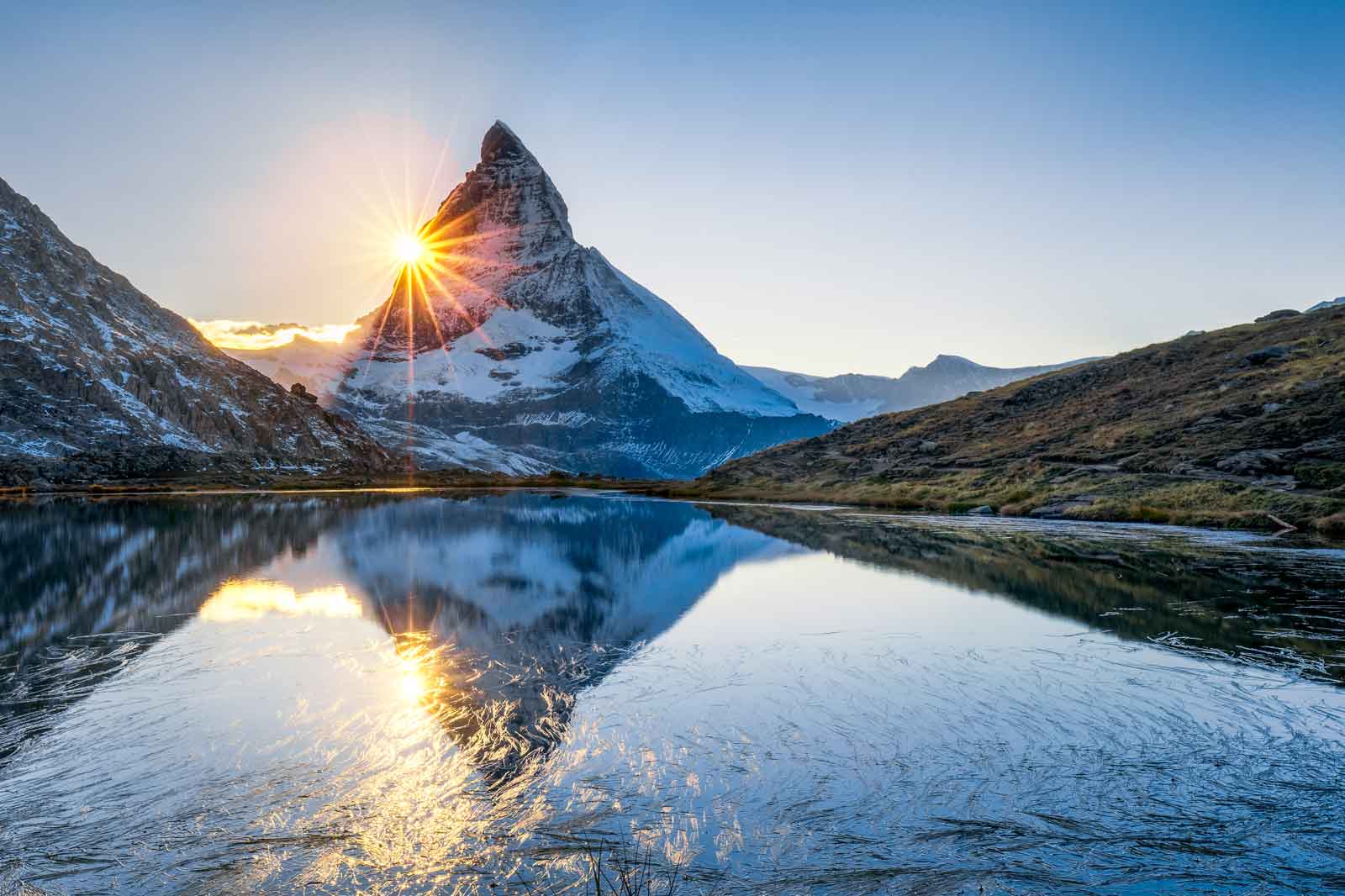 Der Matterhorn-Berg erhebt sich majestätisch im Hintergrund. Sonnenstrahlen blitzen über den Gipfel und spiegeln sich im klaren See.