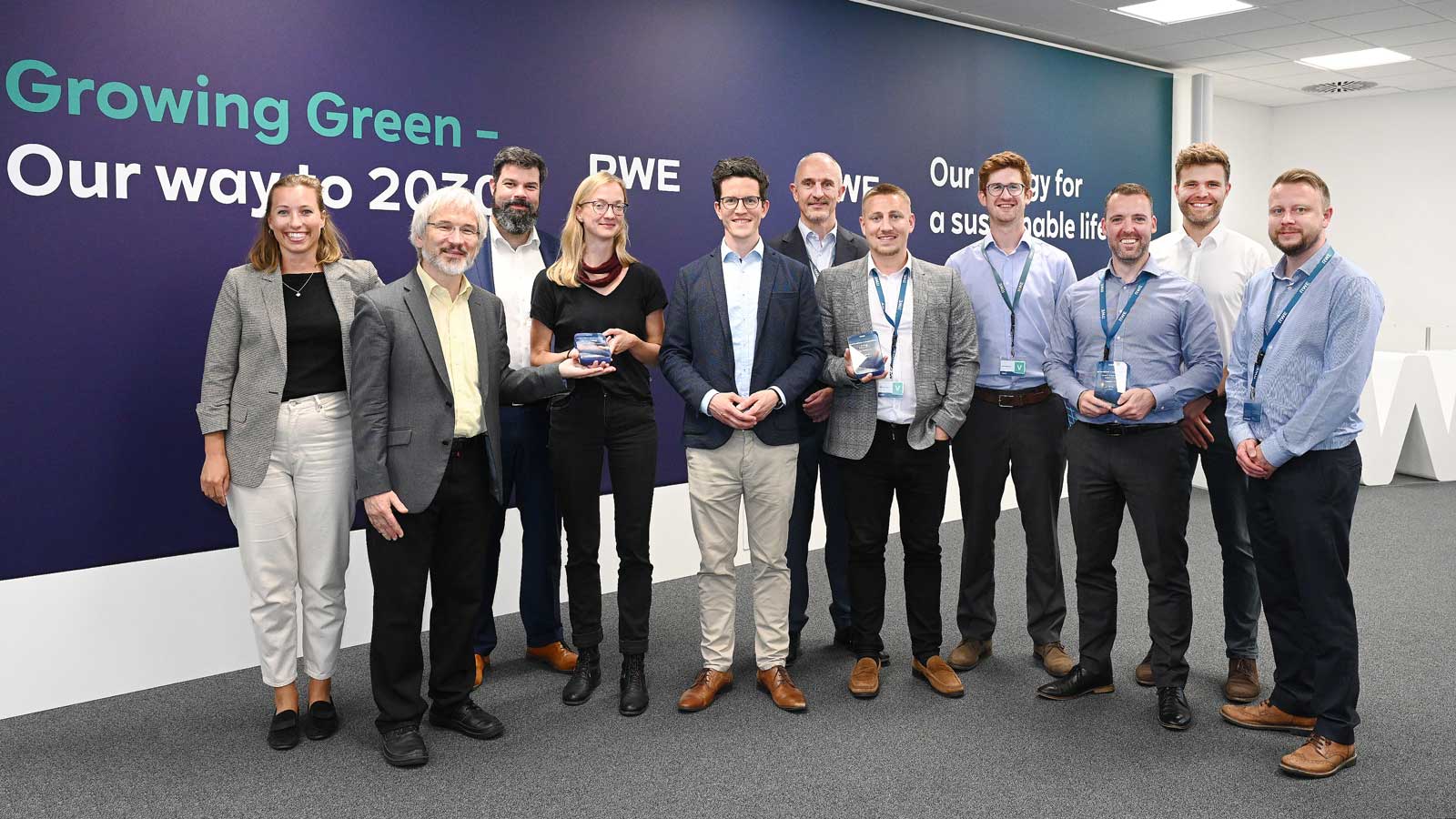 Mehrere Personen stehen zusammen vor einer Wand mit dem Slogan 'Growing Green – Our way to 2030'.