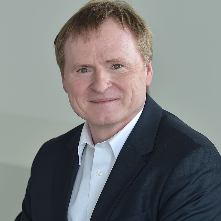 Eine Person in einem Anzug mit einem weißen Hemd sitzt vor einem neutralen Hintergrund. Portrait von Guido Steffen.