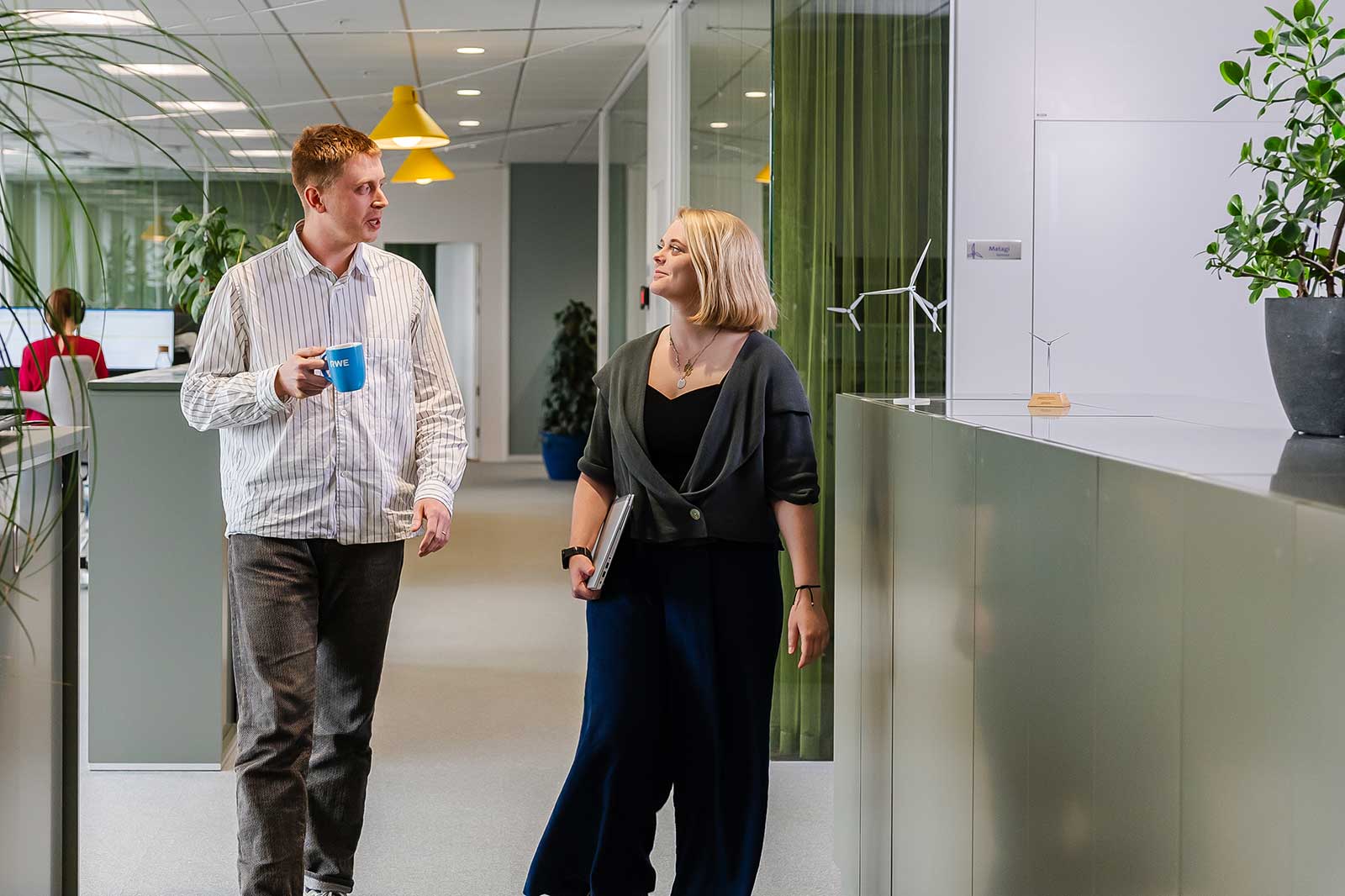 Zwei Personen gehen durch ein modernes Büro mit Pflanzen und farbigen Lampen.