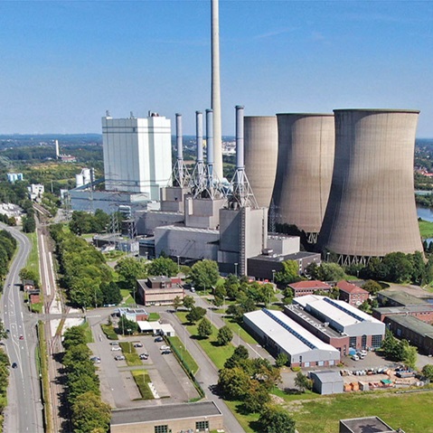 Eine Vogelperspektive auf ein Kraftwerk mit großen Kühltürmen und Industriegebäuden, umgeben von Grünflächen.
