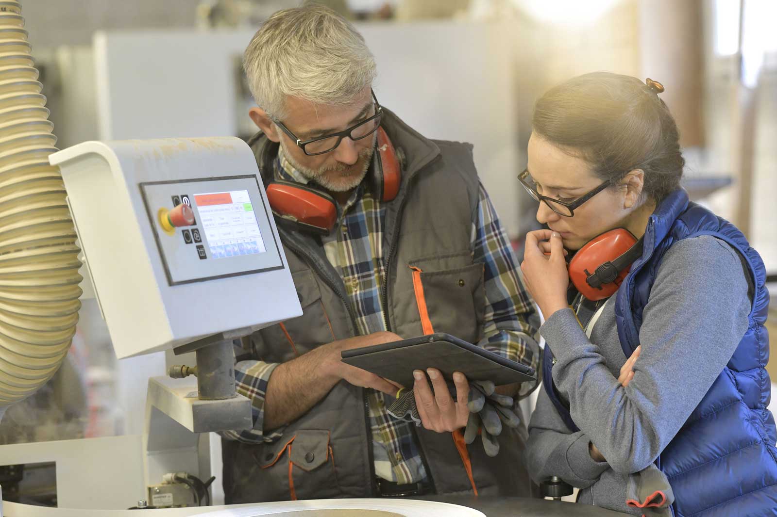 Zwei Arbeiter besprechen die Einstellungen einer Maschine, während sie Daten auf einem Tablet in einer Werkstatt analysieren.