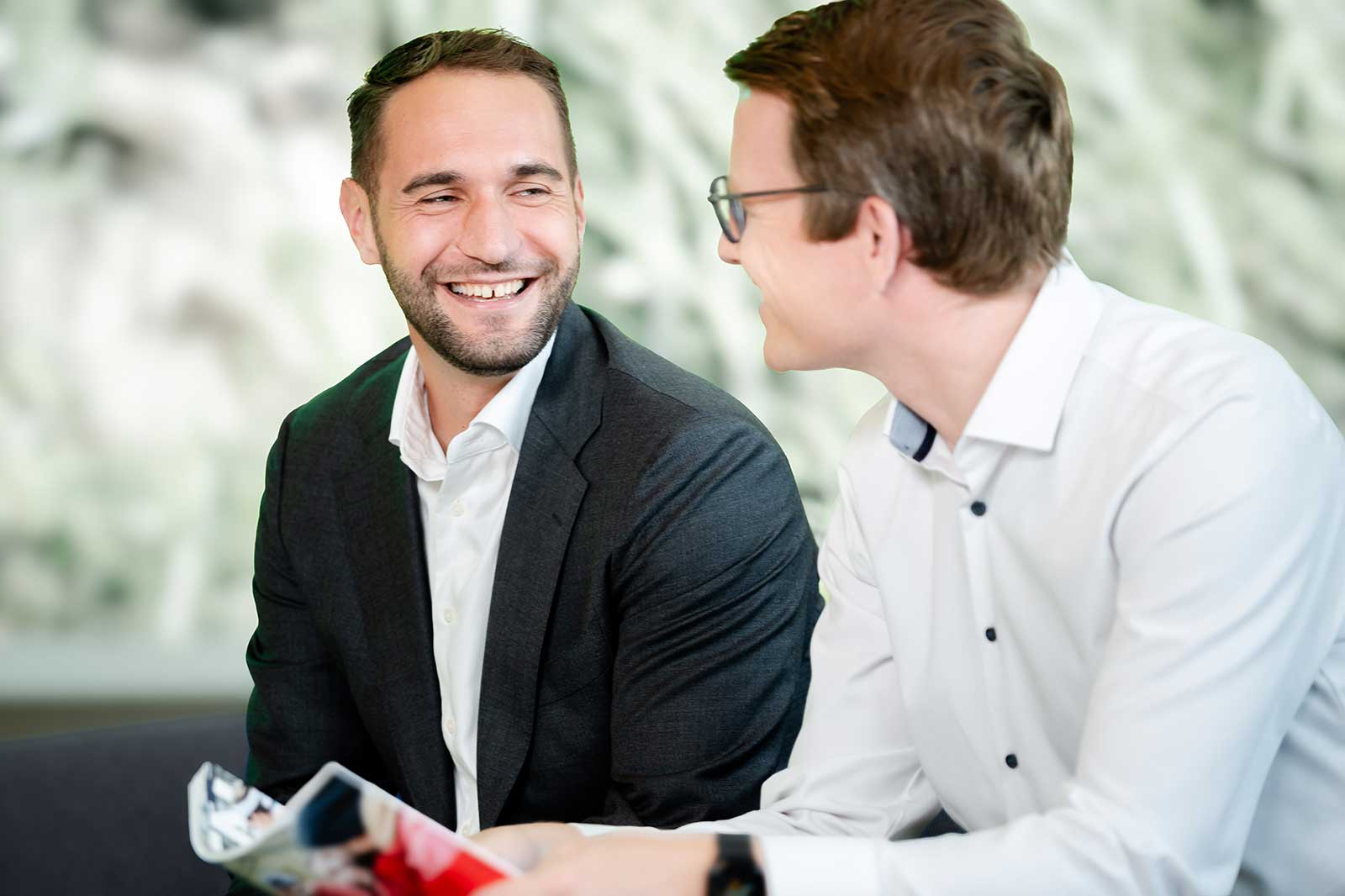 Zwei Männer in formeller Kleidung unterhalten sich in einem modernen Büro mit verschwommenem Hintergrund.