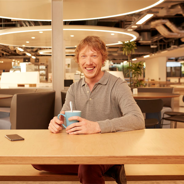 Eine Person sitzt an einem Tisch in einem modernen Café und hält eine blaue Tasse mit einem Löffel darin.