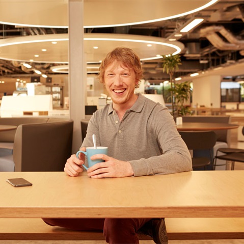 Eine Person sitzt an einem Tisch in einem modernen Café und hält eine blaue Tasse mit einem Löffel darin.