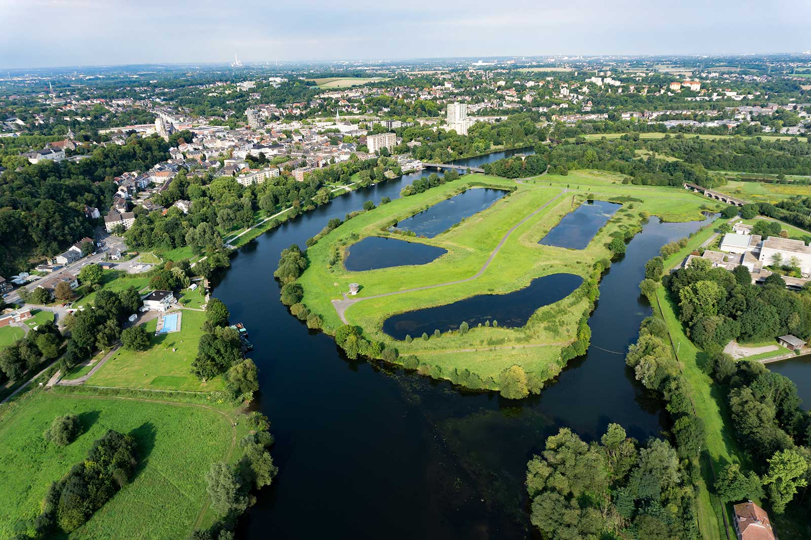 Eine Luftaufnahme einer Stadt mit grünen Flächen, Wasserflächen und einer Mischung aus Wohngebäuden und Bäumen.
