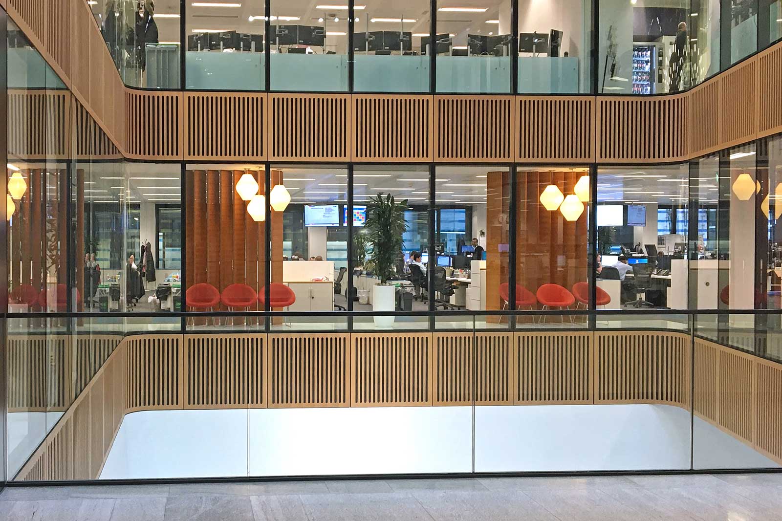 Ein modernes Bürogebäude mit großen Fenstern, Holzelementen, rot-orangefarbenen Stühlen und mehreren Arbeitsplätzen.