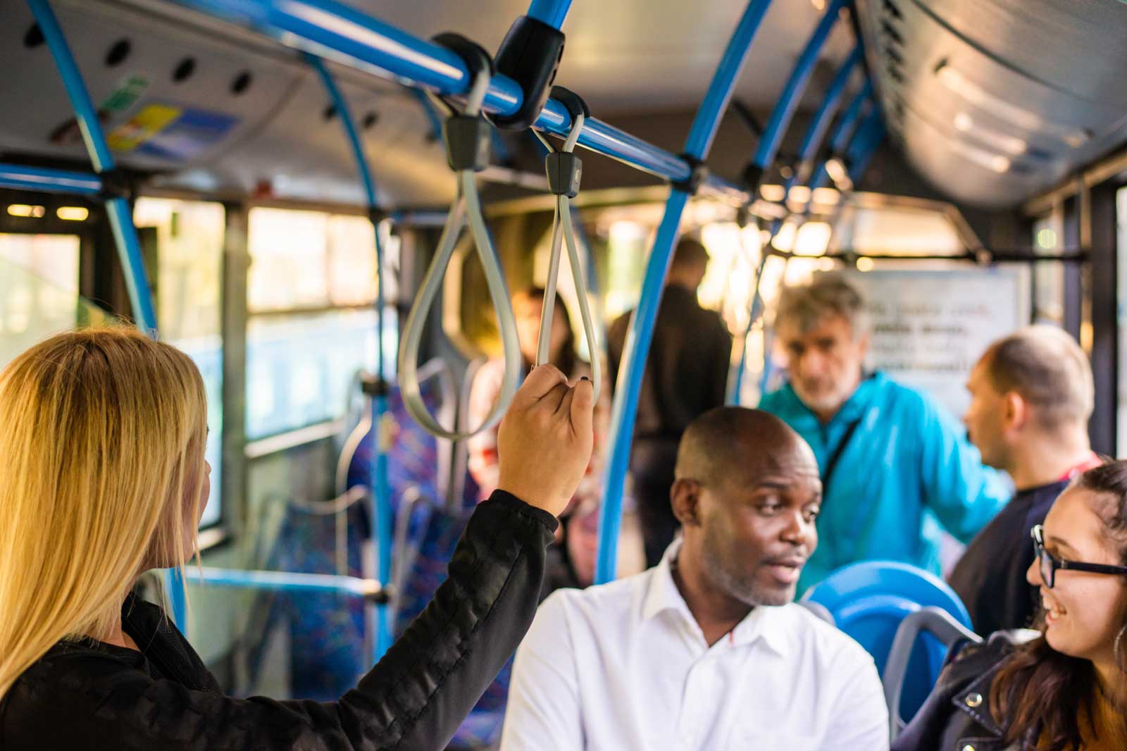 Eine Person hält sich am Haltegriff in einem Bus fest, während andere Fahrgäste sitzen.