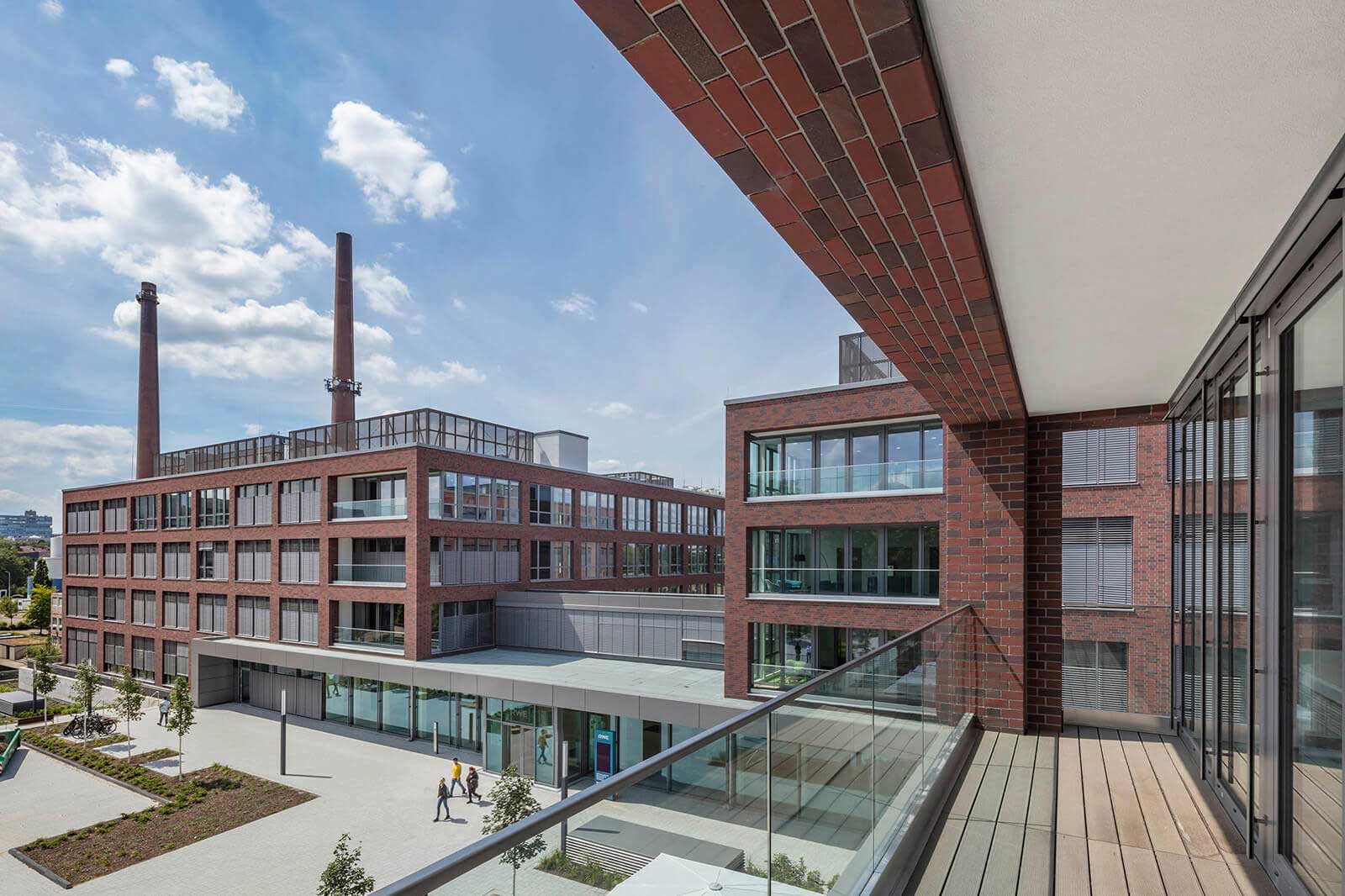Ein Blick auf moderne Backsteingebäude mit großen Fenstern und rauchenden Schornsteinen unter einem blauen Himmel.