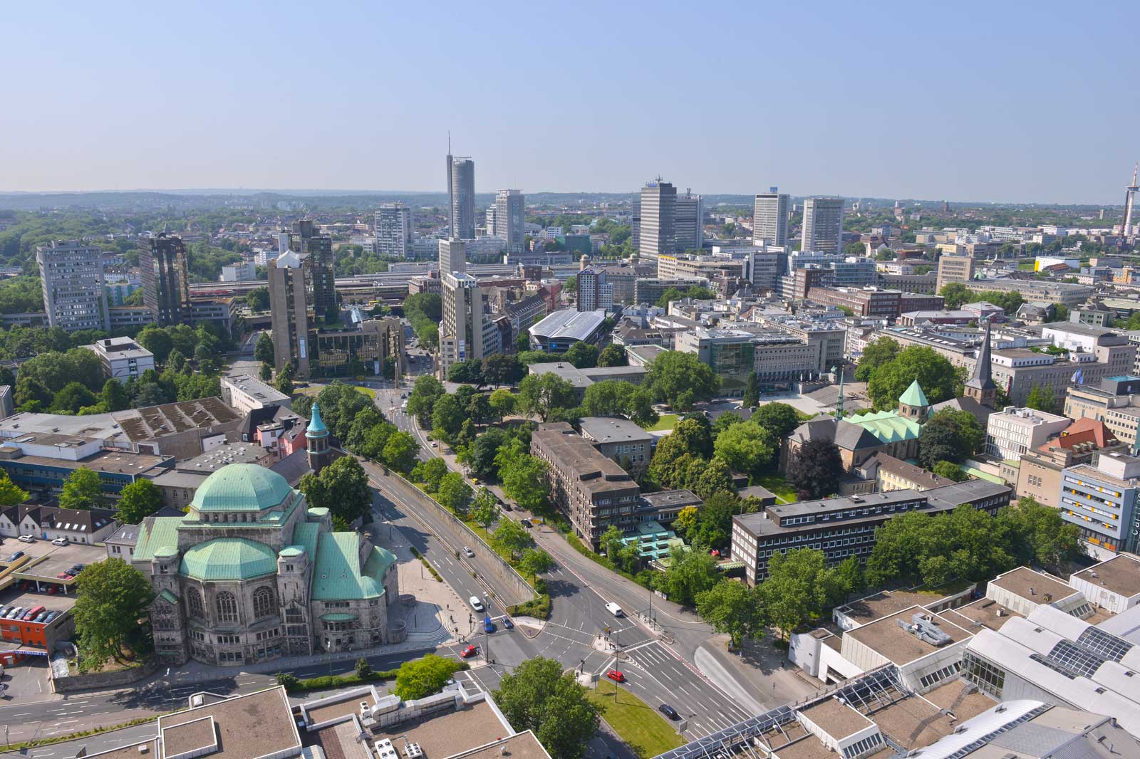 Luftaufnahme einer modernen Stadt mit Grünflächen, Gebäuden und einer markanten Kuppelstruktur mit grünem Dach.