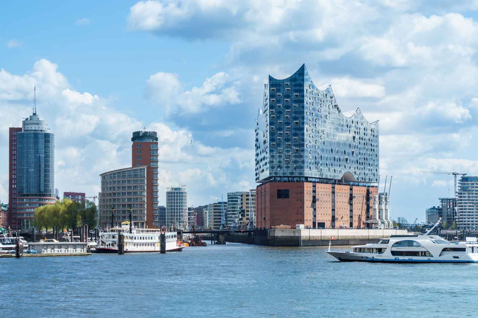Die Elbphilharmonie in Hamburg, umgeben von modernen Gebäuden und Booten im Wasser, unter einem bewölkten Himmel.