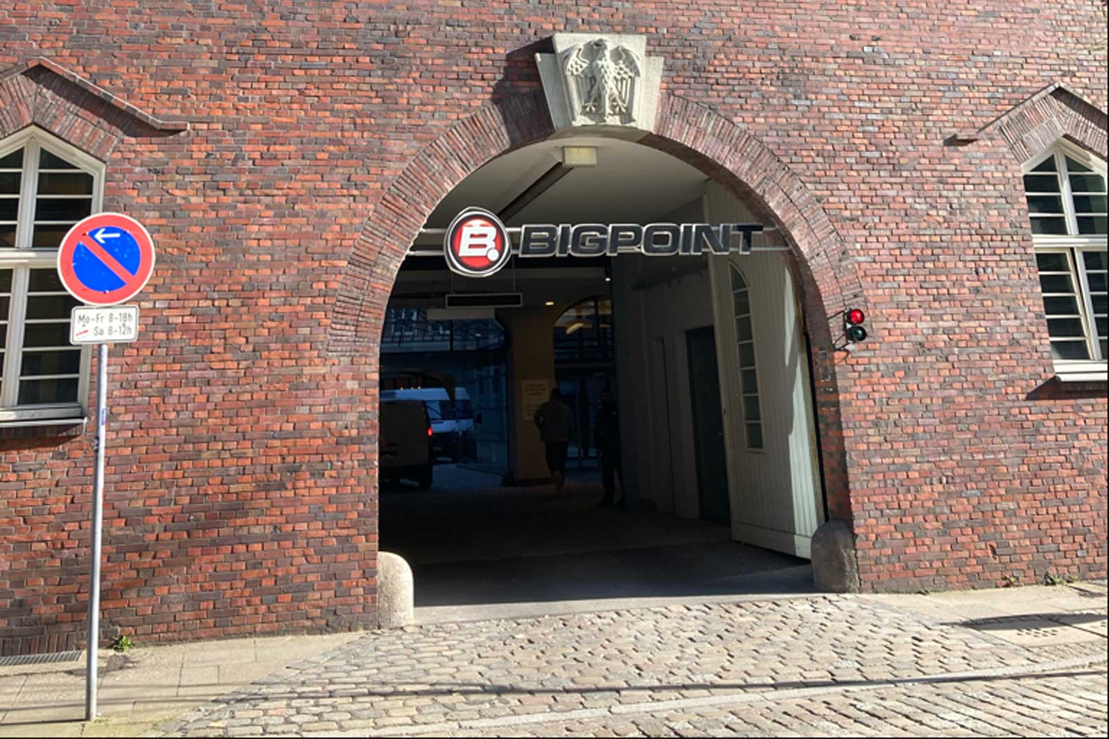 Ein Backsteintor mit dem Schriftzug 'BIGPOINT'. Verkehrsschilder sind sichtbar, sowie ein rotes Licht im Eingang.